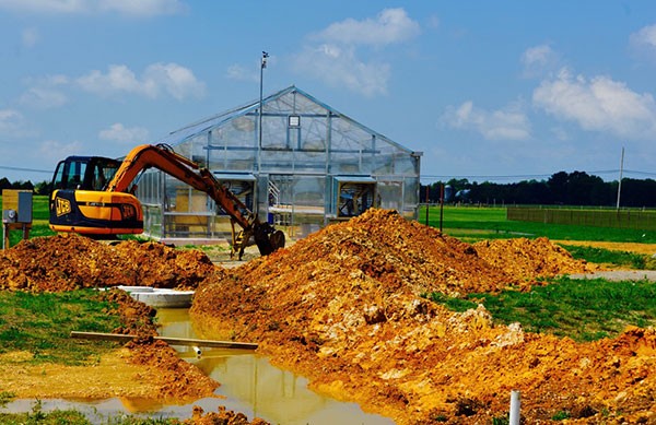 greenhouse with backhoe digging a trench and mounds of soil