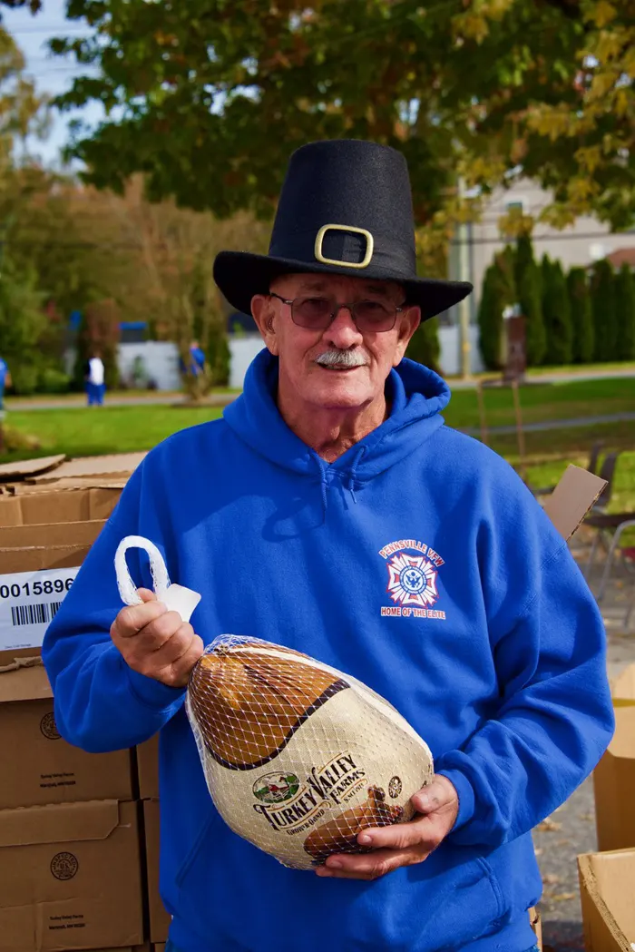 Volunteer wearing thanksgiving hat holding a frozen turkey